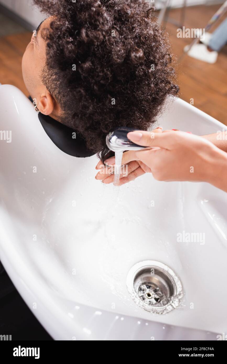 Hairdresser holding shower near african american client in salon Stock