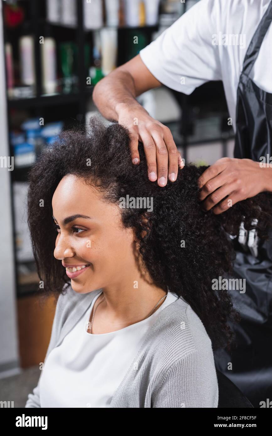 Cheerful african american woman sitting near hairdresser in salon Stock
