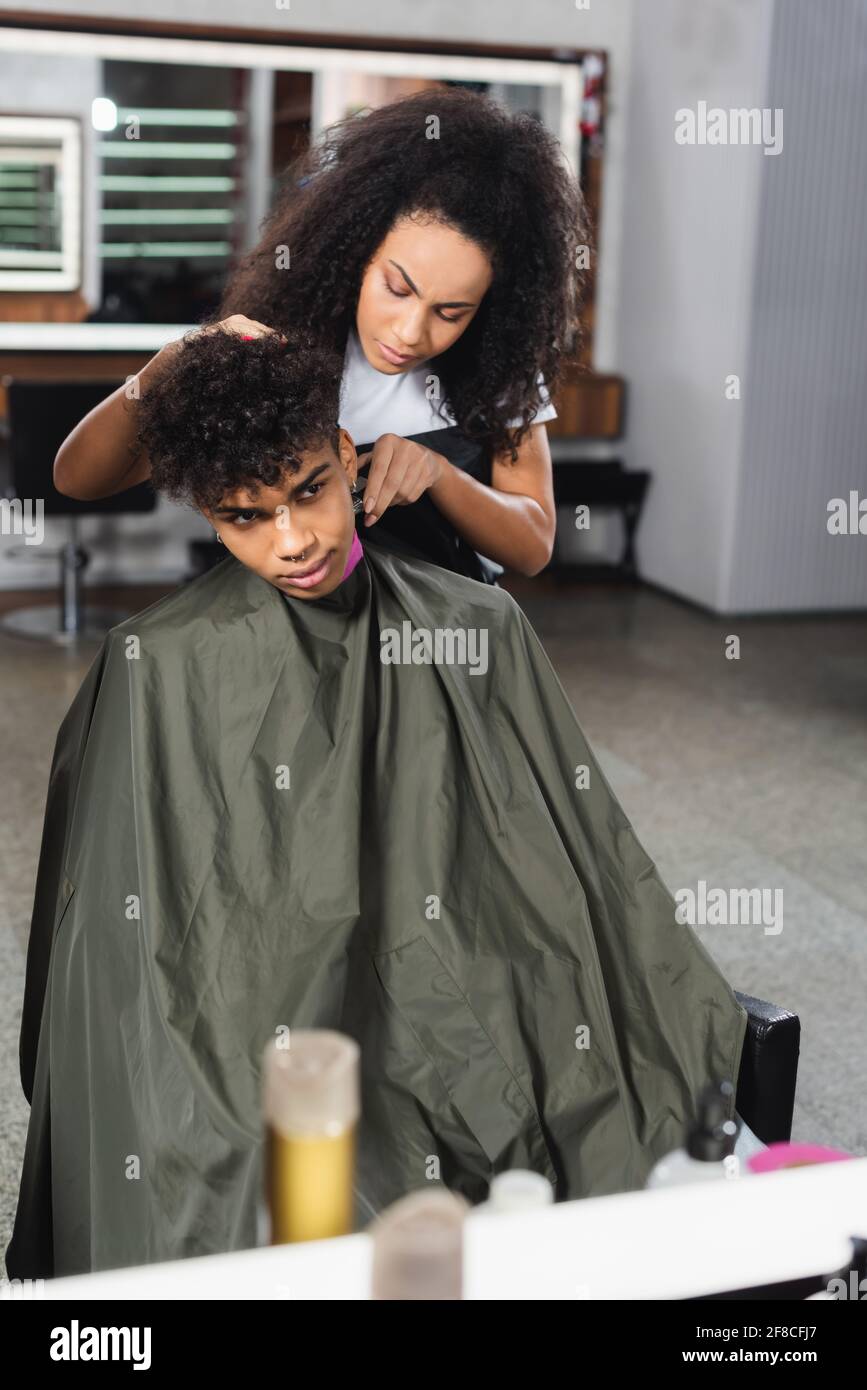African american hairdresser trimming neck of client in cape in salon