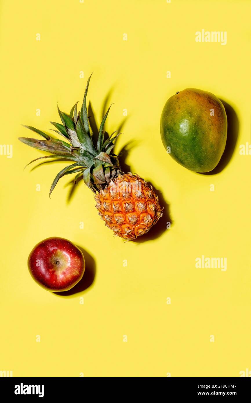 Mini pineapple, mango and apple on a solid yellow background Stock Photo