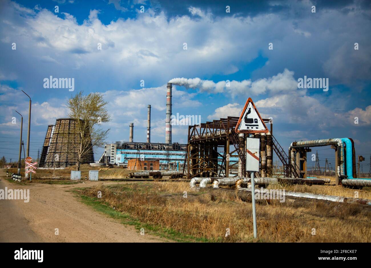 Power station with cooling towers and smocking factory chimneys. hand-made railroad sign 'Warning, Train!' Blue sky, clouds. Kazakhstan, Stepnogorsk. Stock Photo