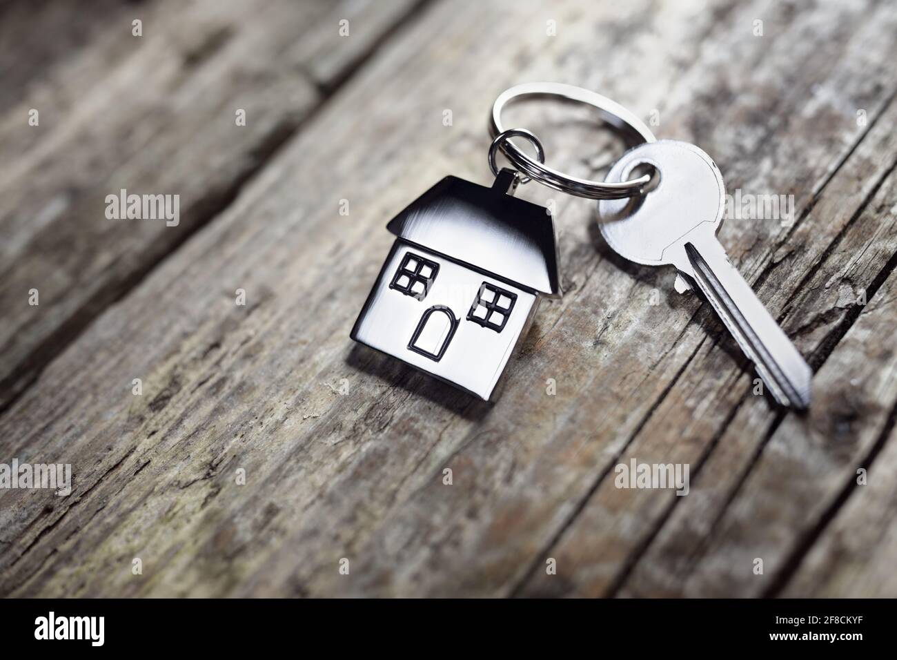 House key on a house shaped keychain resting on wooden floorboards concept for real estate, moving home or renting property Stock Photo