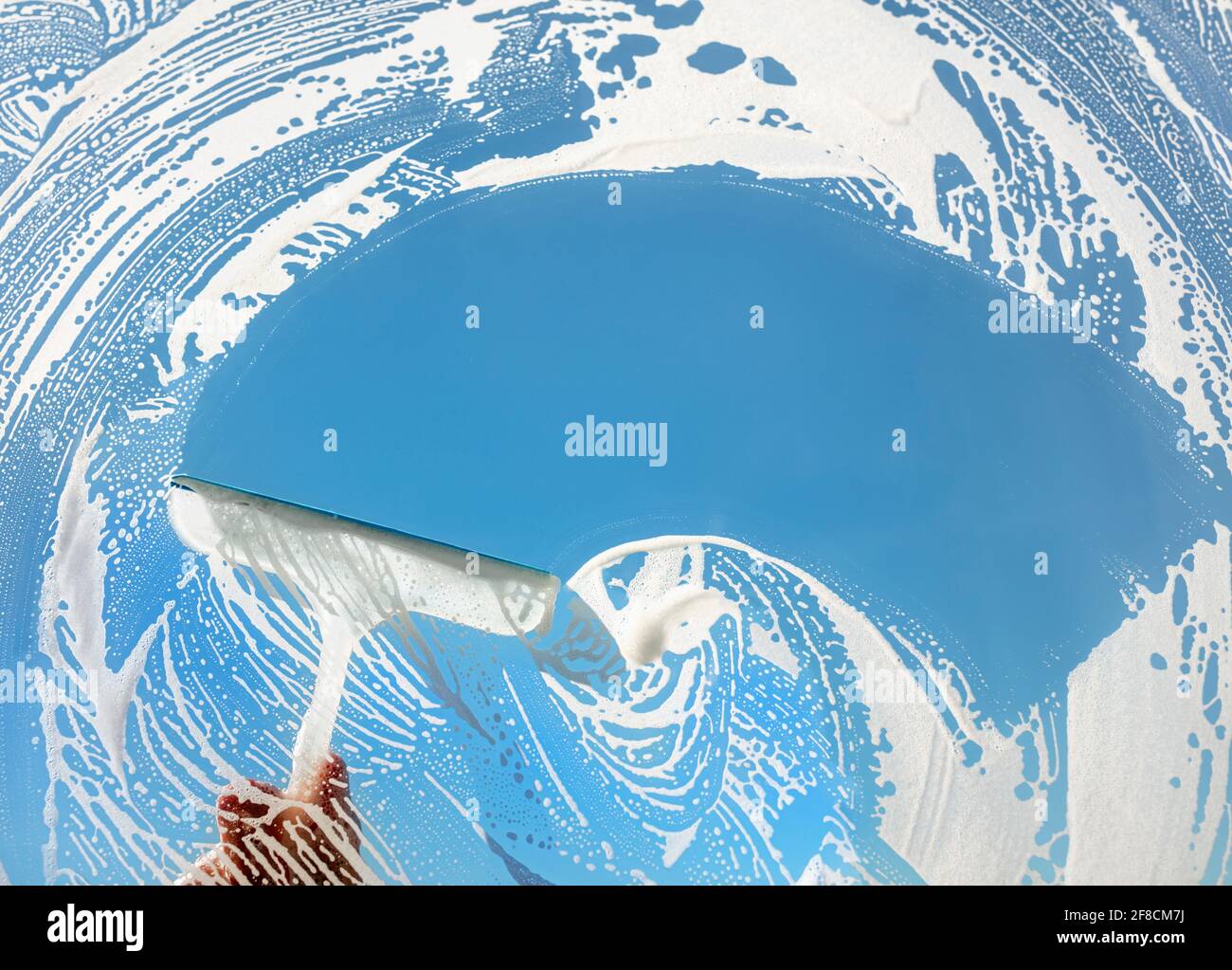 Window cleaner using a squeegee to wash a window with clear blue sky Stock Photo