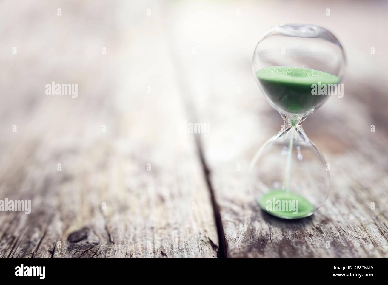 Green hourglass on wood background concept for time or ecology and environmental conservation Stock Photo