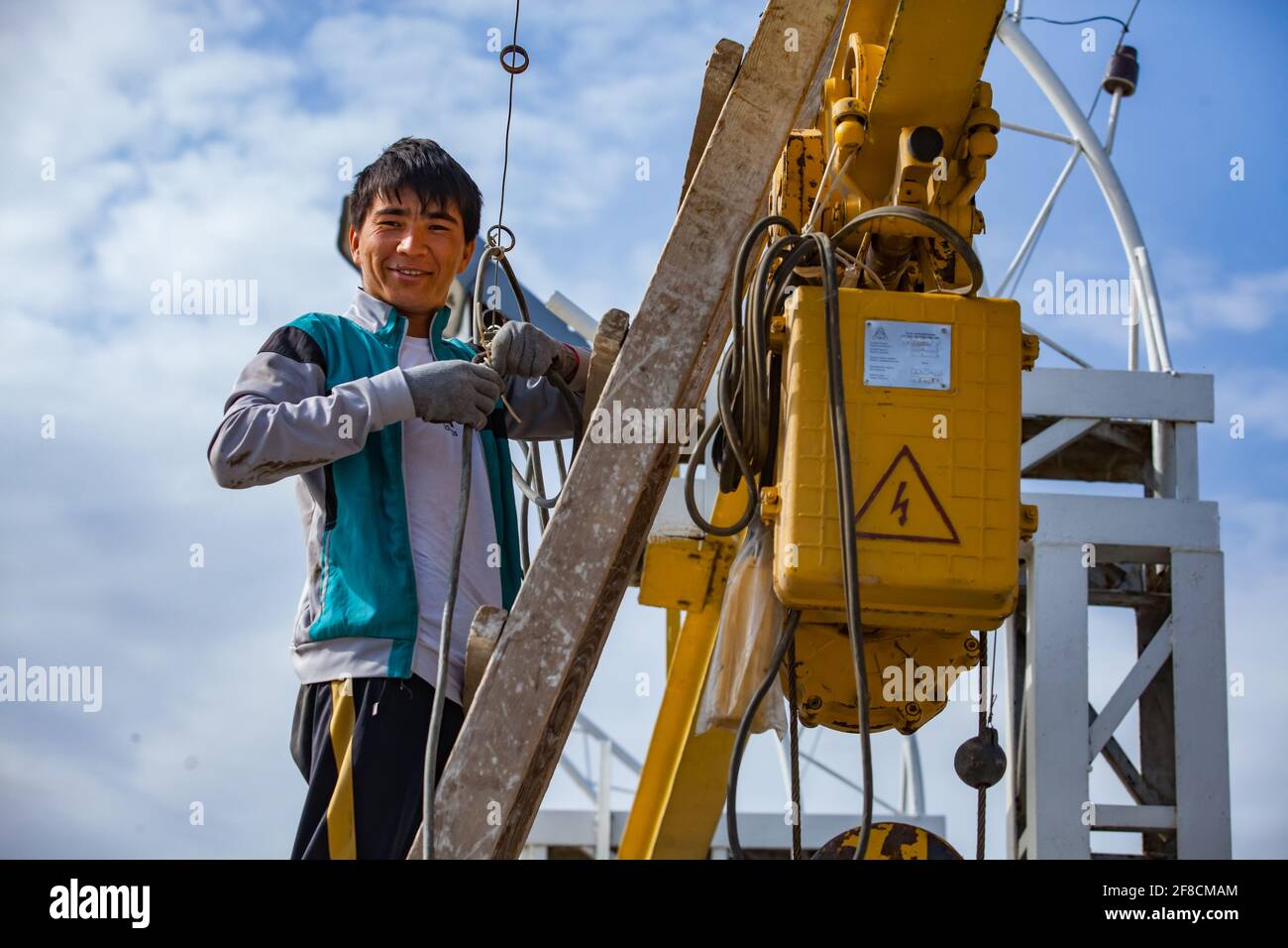 Kazakhstan, Shardara water storage dam. Asian (Uzbek) electrician worker fixing lifting device. Renovation of water shutter winch (crane). Stock Photo