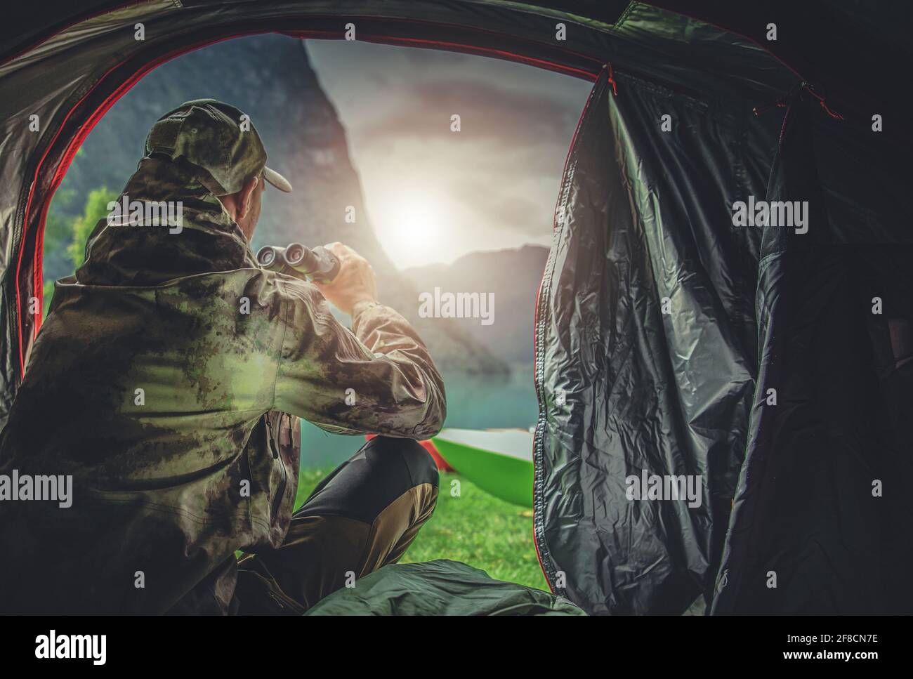 Caucasian Hunter in His 40s Spotting Wildlife Using Professional Binoculars Straight From His Hunting Spot Tent. Hunting Season Theme. Stock Photo