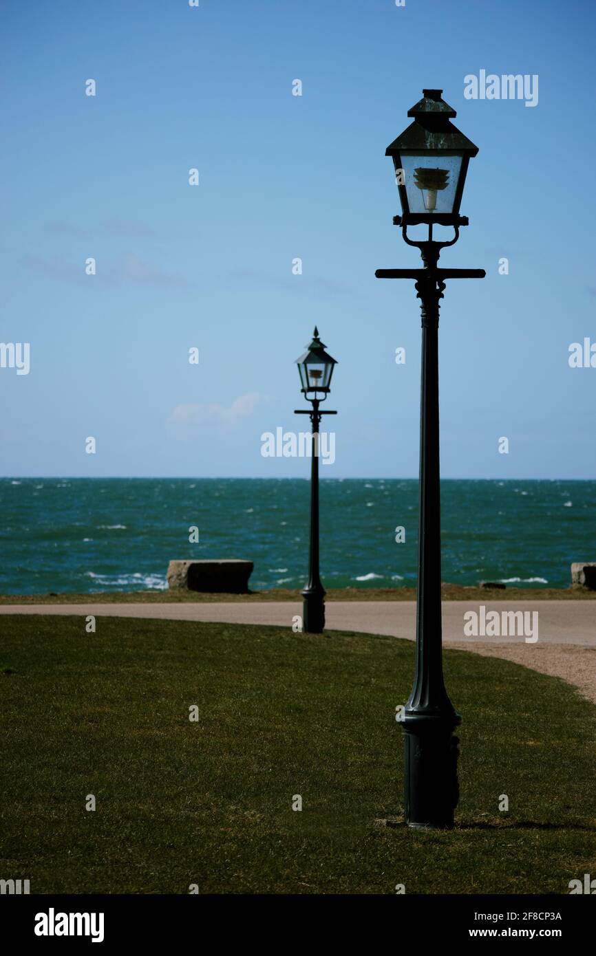 Two street lamps in vintage style on the dark green lawn with a turquoise sea in the background and distinct horizon line. Stock Photo