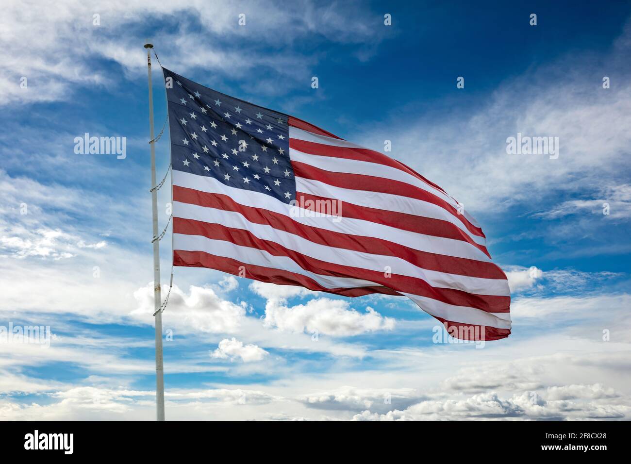 United States of America flag on a pole waving against blue cloudy sky ...