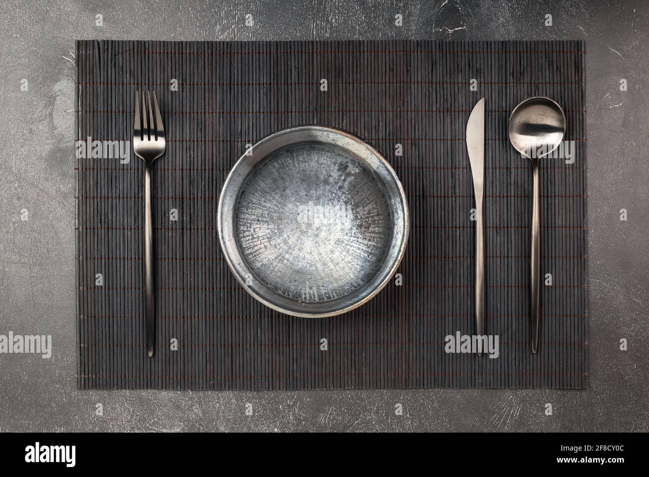 Empty black clay plate and sblack metal silverware set on wooden table Stock Photo