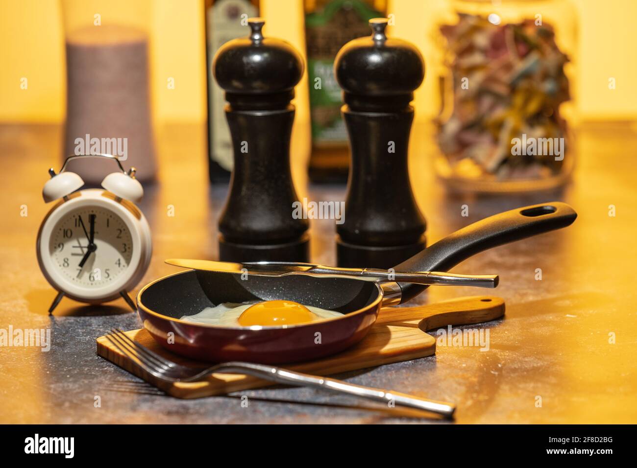 Fried egg in a pan standing on the kitchen table next to the alarm clock. Breakfast in preparation Stock Photo