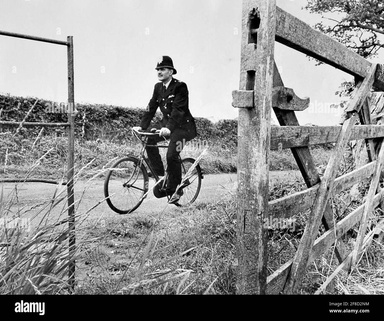 Rural village policeman riding bicycle while patrolling his beat Britain 1965 Uk England 1960s police constable officer cycling bike riding country lane Stock Photo