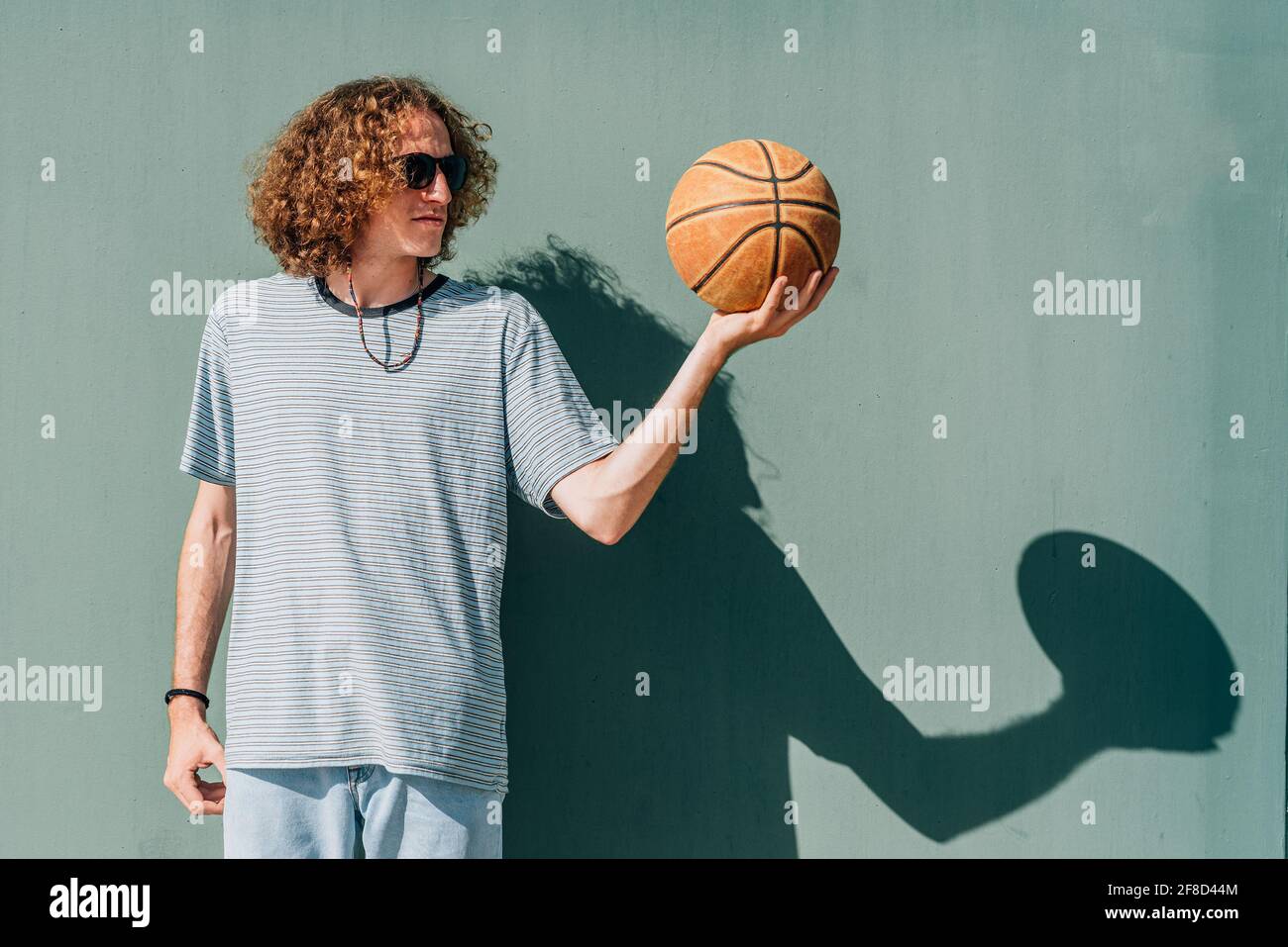 attractive young man looking to the basketball ball he holds with one hand. He dresses casual and wears sunglasses Stock Photo
