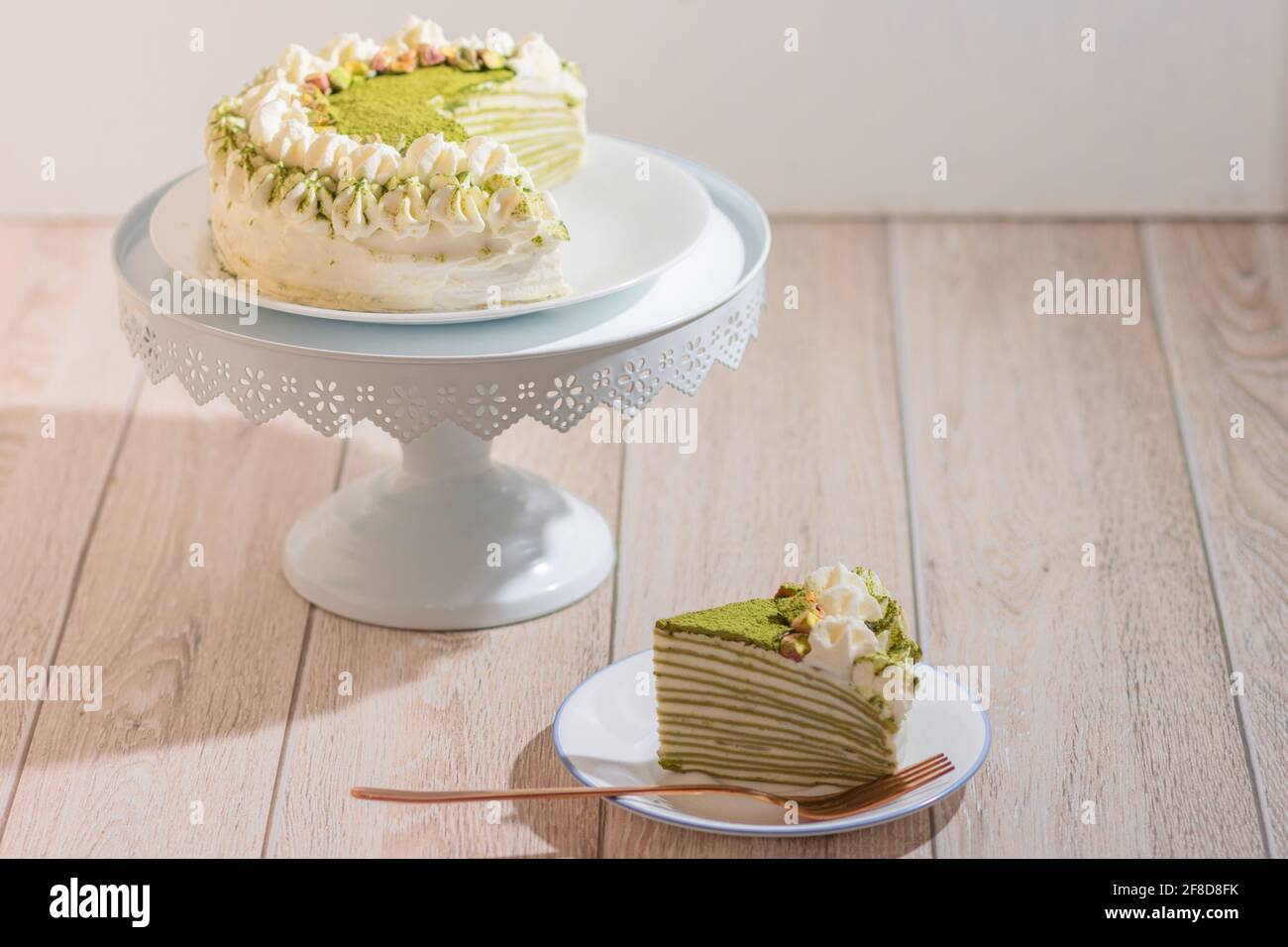 Matcha Mille Crepe Cake Presented On A Cake Holder With A Slice On A Plate Stock Photo
