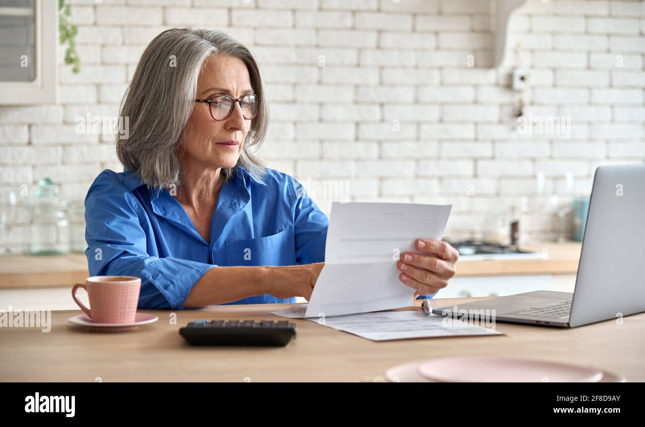 Senior mid 60s aged woman calculating bank fee with computer. Stock Photo