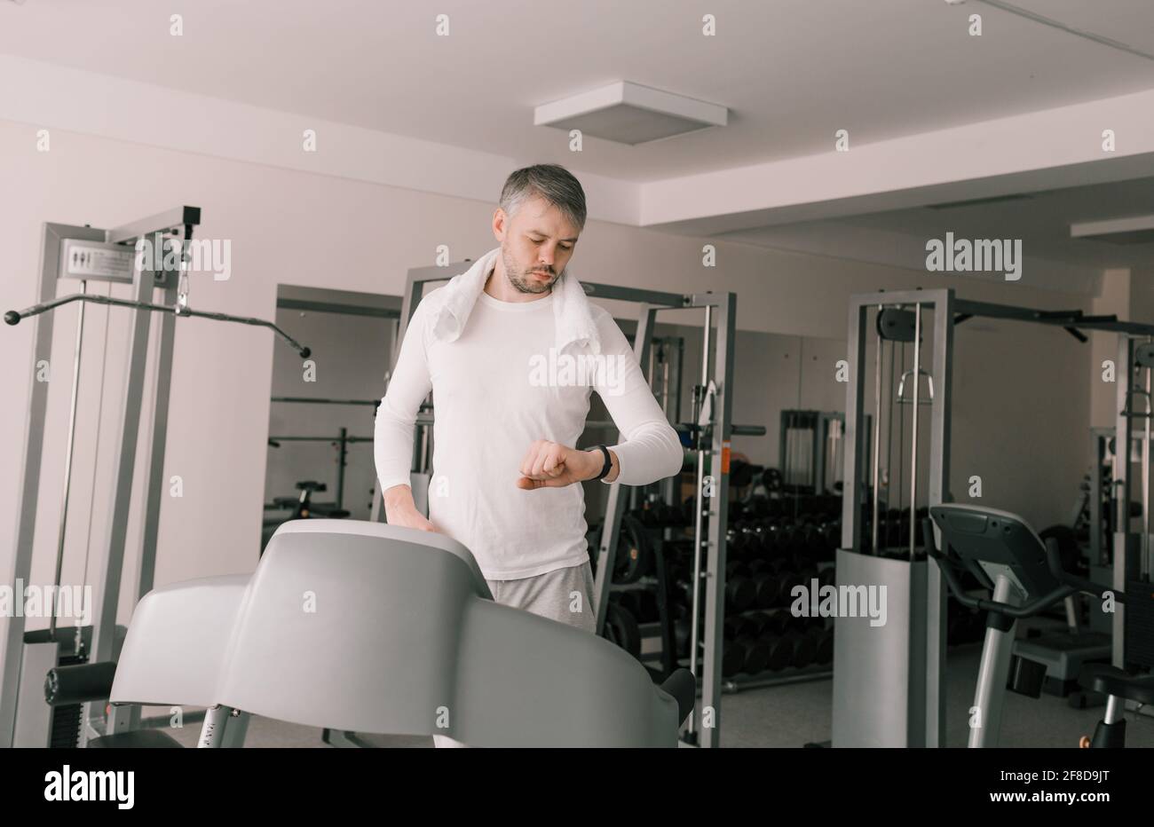 a man stands on a treadmill and carefully looks at the clock after a cardio workout. Taking care of your body. Stock Photo