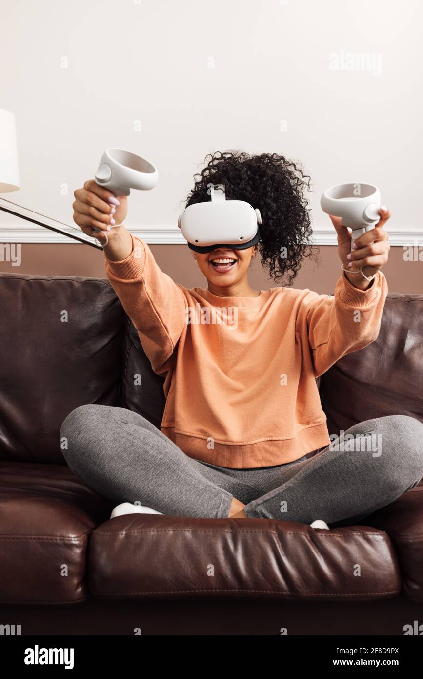 Young happy woman sitting on couch using VR Stock Photo