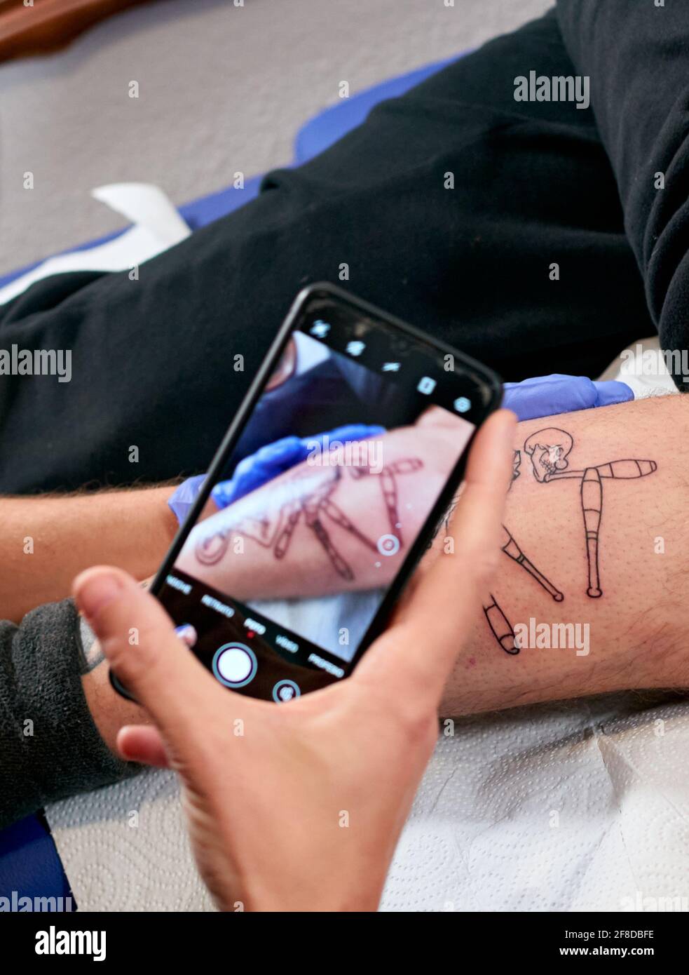 Hand taking a photo with a phone of the skeleton tattoo in a suit on a wheel Stock Photo