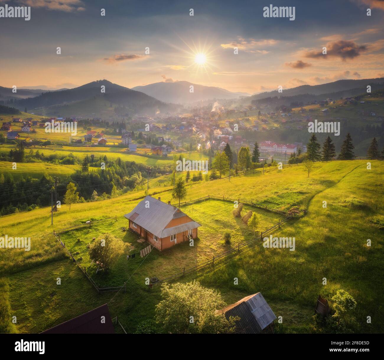 Aerial view of beautiful village in Carpathian mountains at sunset in summer. Colorful landscape with green meadows, houses with gardens, trees, sky w Stock Photo