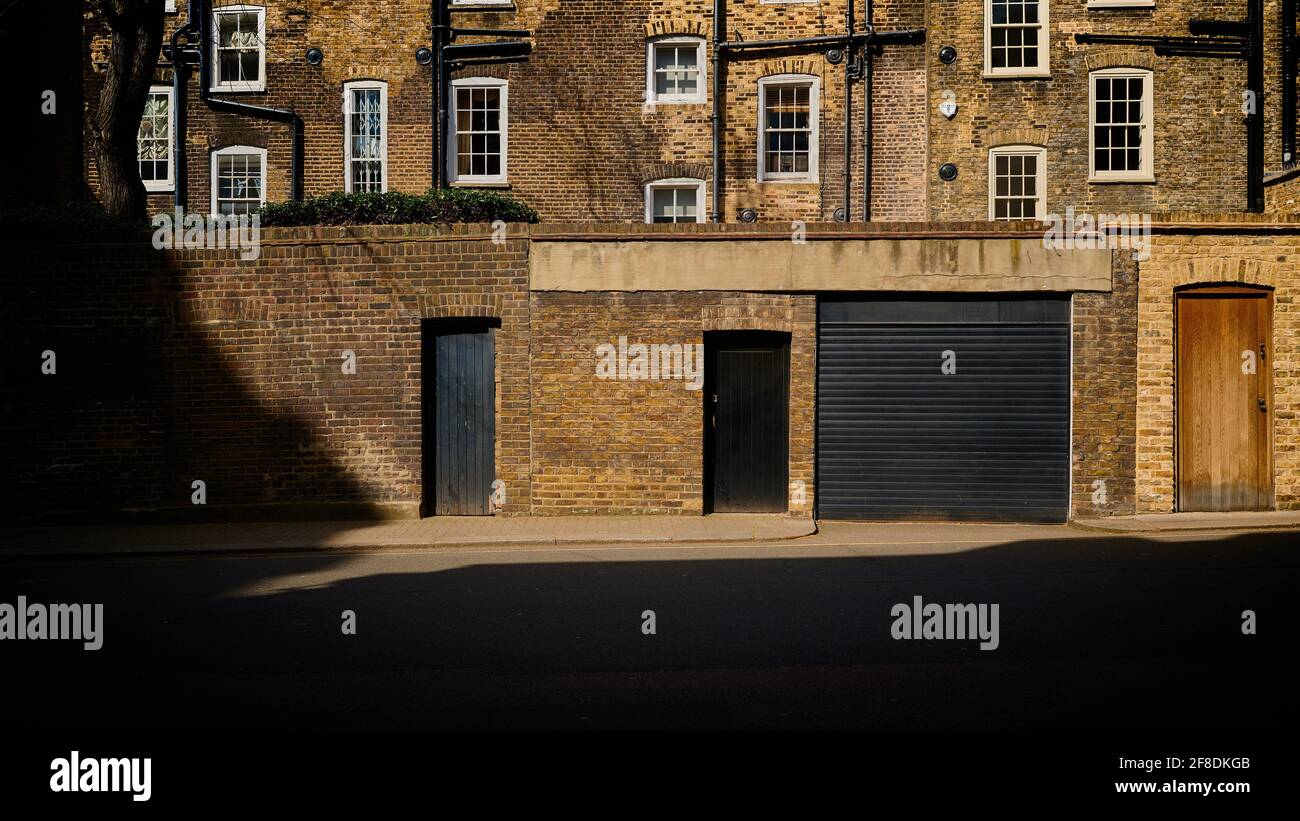 Rows of windows and doors at rear of old victorian terraced houses in london with black drainpipes and long shadows Stock Photo