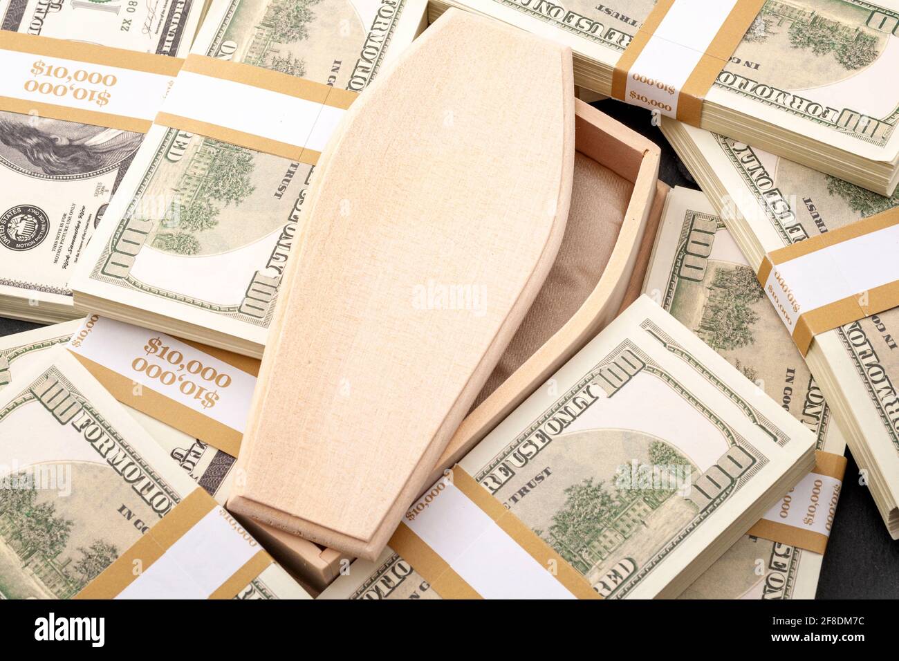 Buried in debt, funeral costs and money problems concept with close up on wooden coffin or casket and bundles of cash (US dollars) Stock Photo