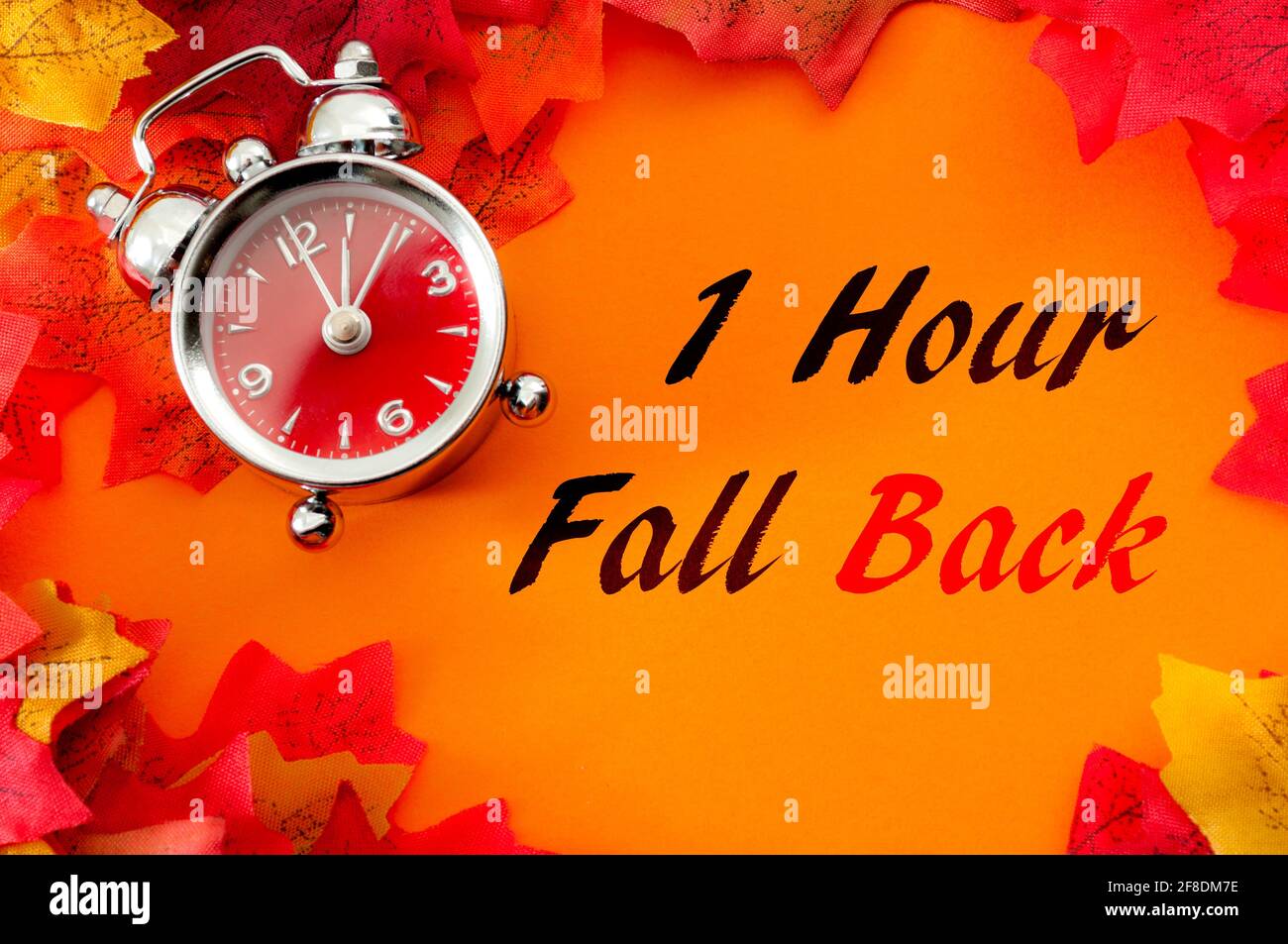 Fall back, the end of daylight savings time and turn clocks back on hour concept with a clock surrounded by dried yellow leaves with the text One hour Stock Photo