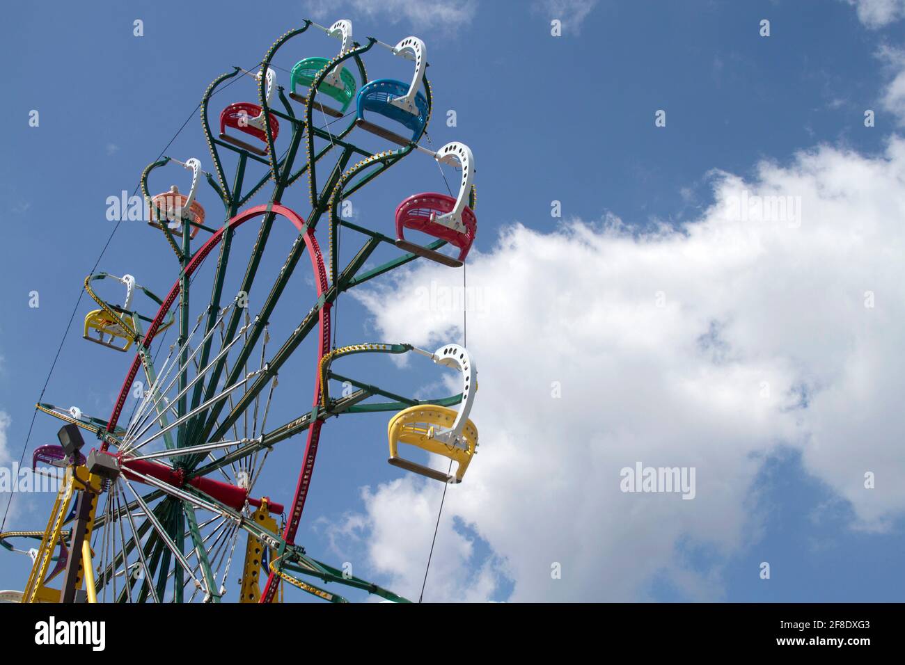 A Families have fun riding a colorful ferris wheel up, down and around through a blue skiy and clouds on a summer day Stock Photo