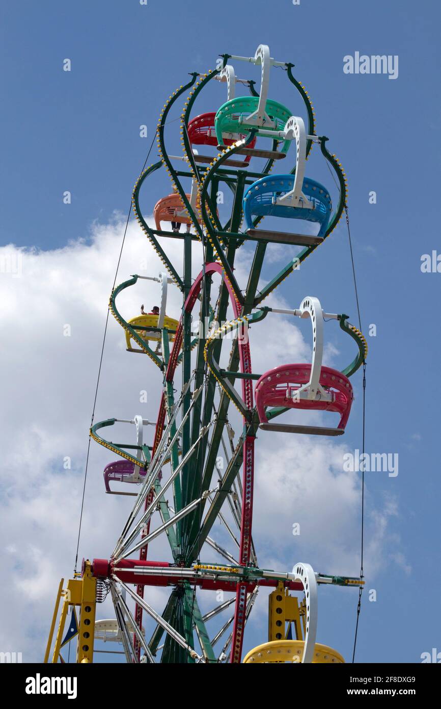 A Families have fun riding a colorful ferris wheel up, down and around through a blue skiy and clouds on a summer day Stock Photo