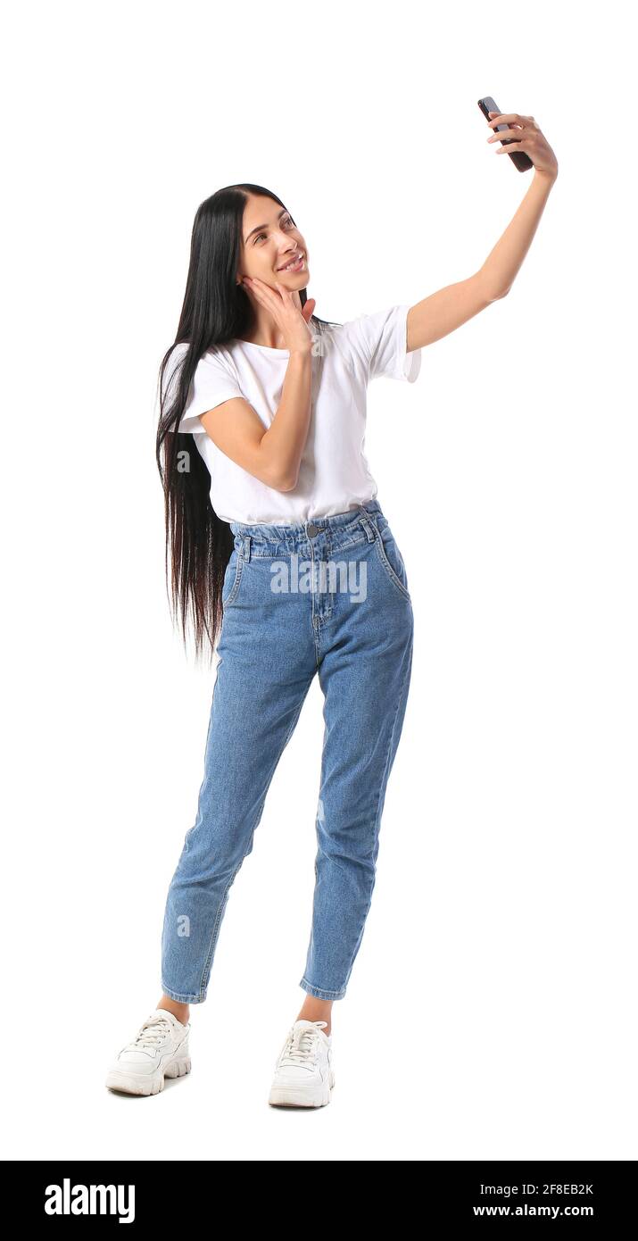 Beautiful young woman with mobile phone taking selfie on white ...