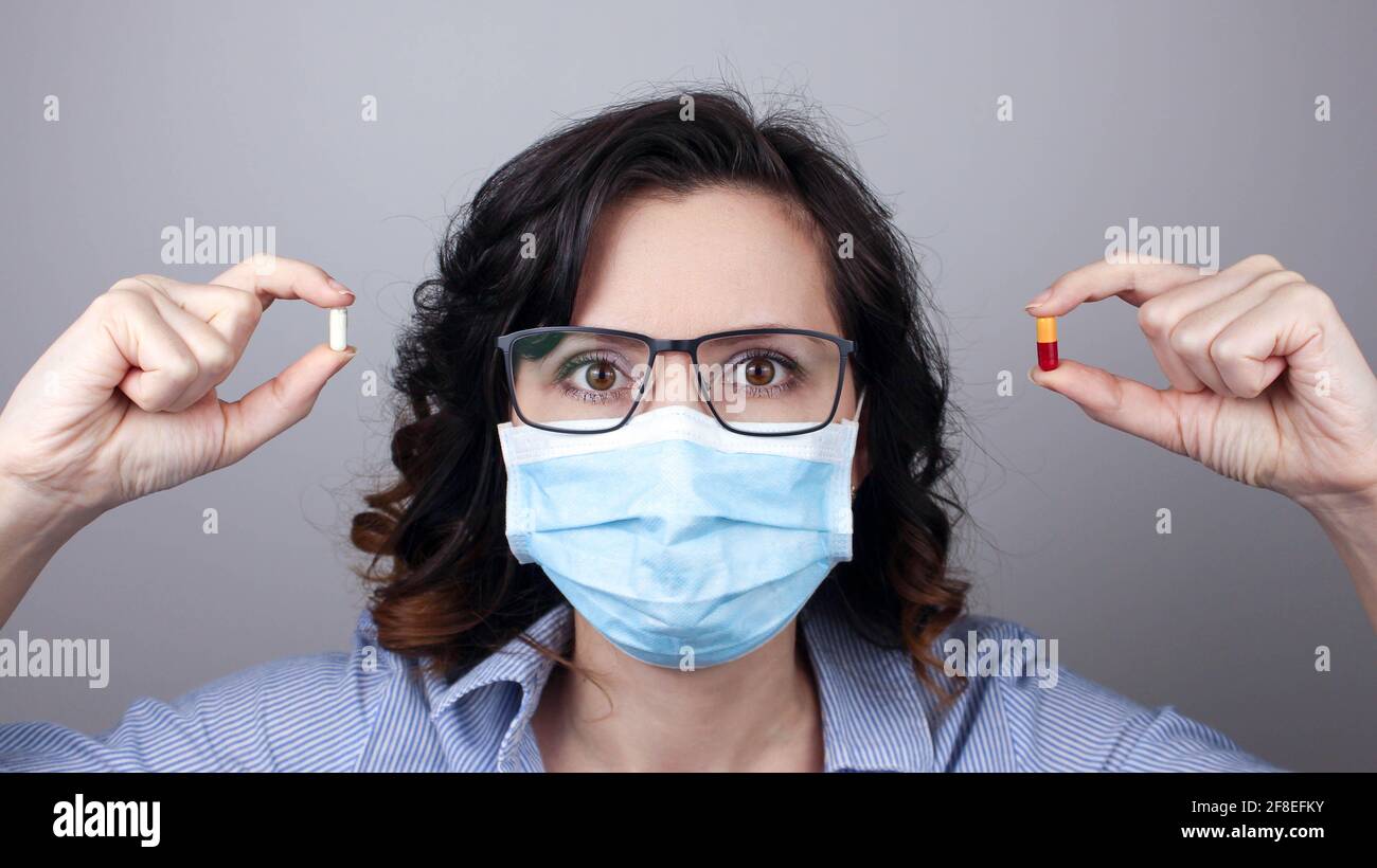 Woman wearing protection face mask against coronavirus and glasses. Woman in a mask showing medicine pill, vaccine. Medical mask, Close up shot, Selec Stock Photo