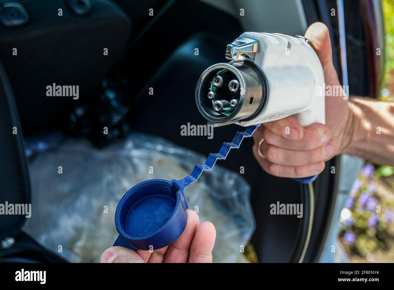 Charging device for an electric car in the man's hand against the background of an open trunk.  Stock Photo