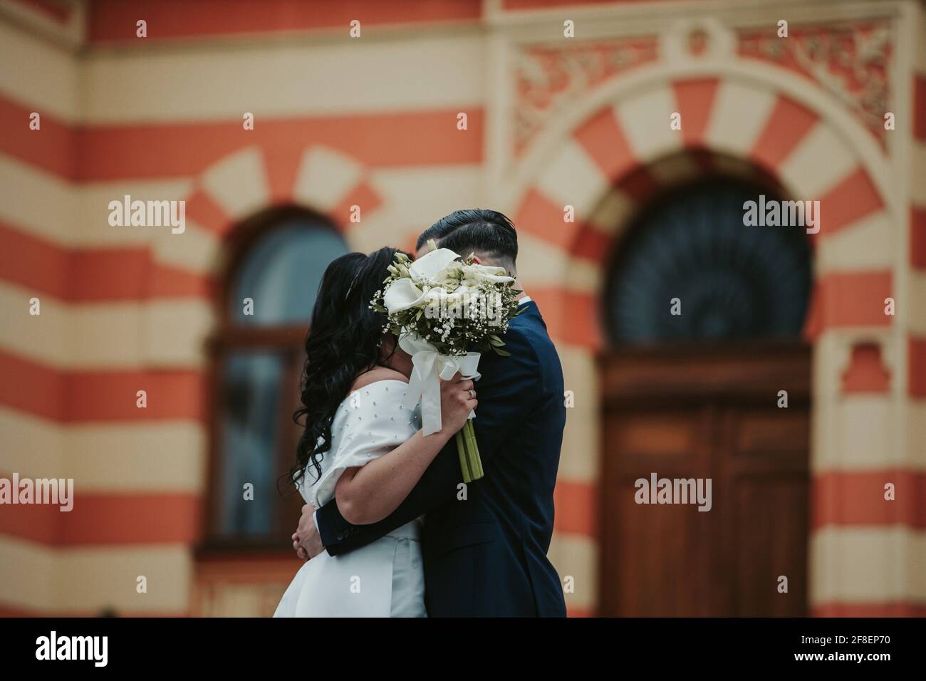 Bride and groom kissing outdoors hiding behind a flower bouquet Stock ...