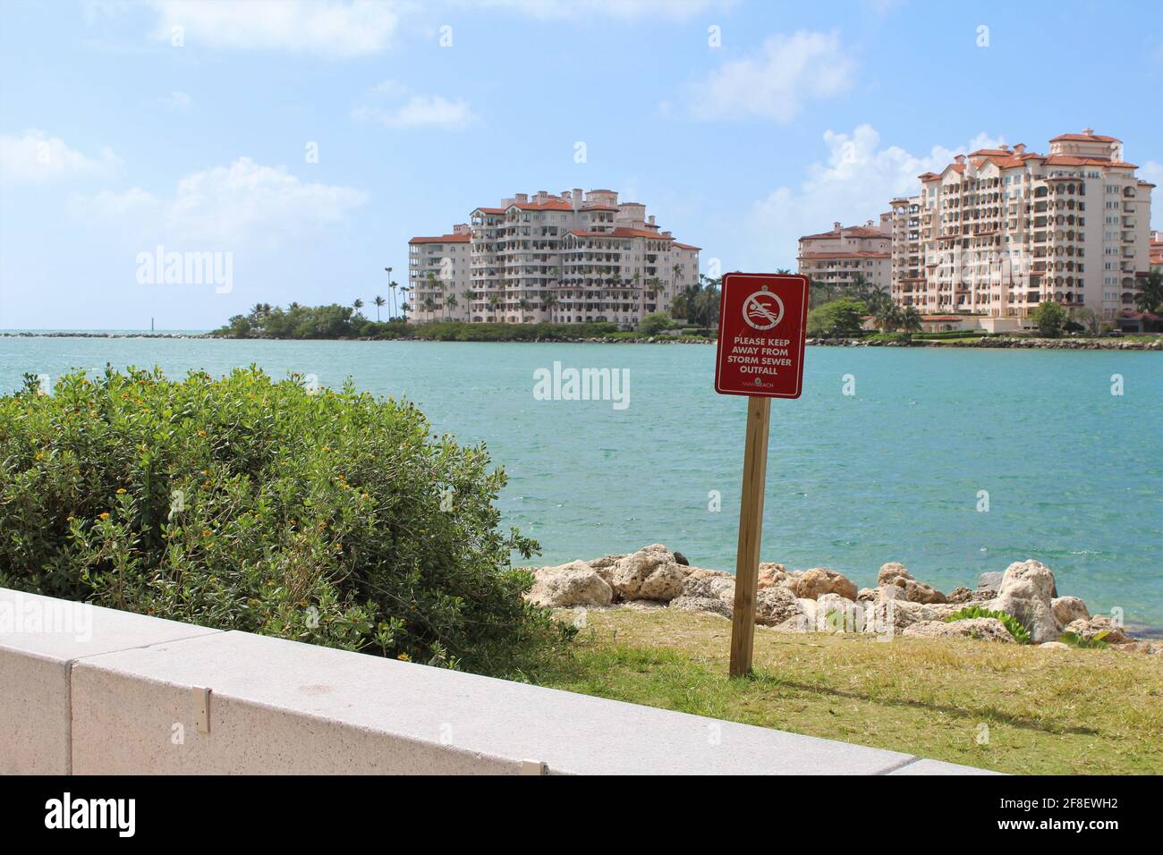 Sign to keep away from storm sewer at South Pointe beach in Miami Beach Florida with a background view of Palazzo Del Sol condominiums in Fisher Island Stock Photo