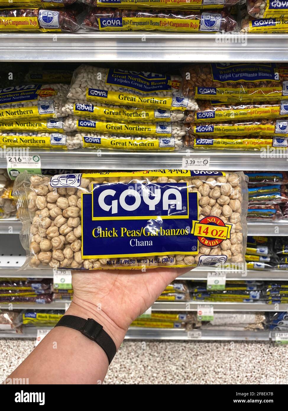 Goya brand beans and other foods in a grocery store aisle. Person holding GOYA chickpeas bag in hand. Stock Photo