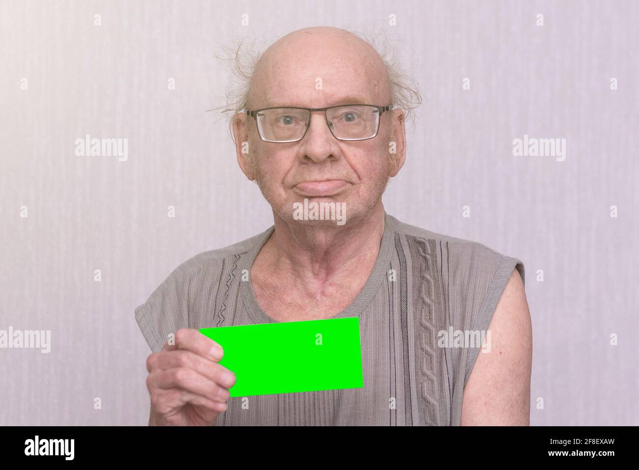 Old retired bald man with eyeglasses in gray shirt is blank in his hand. Stock Photo