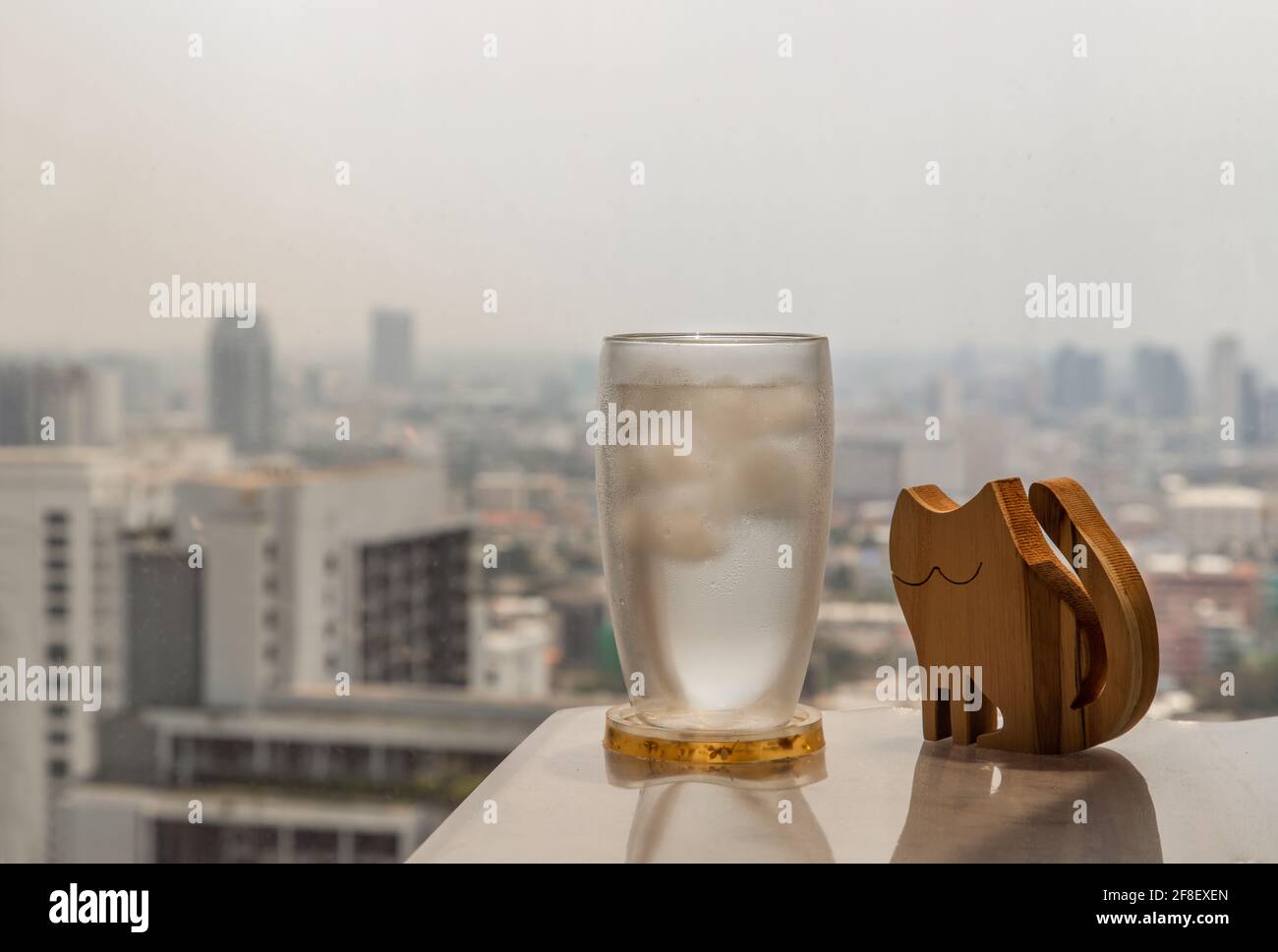 Glass of refreshing water drink with ice and wooden doll cat shape on white  table in living room with city view. Place for text or advertising, Select  Stock Photo - Alamy