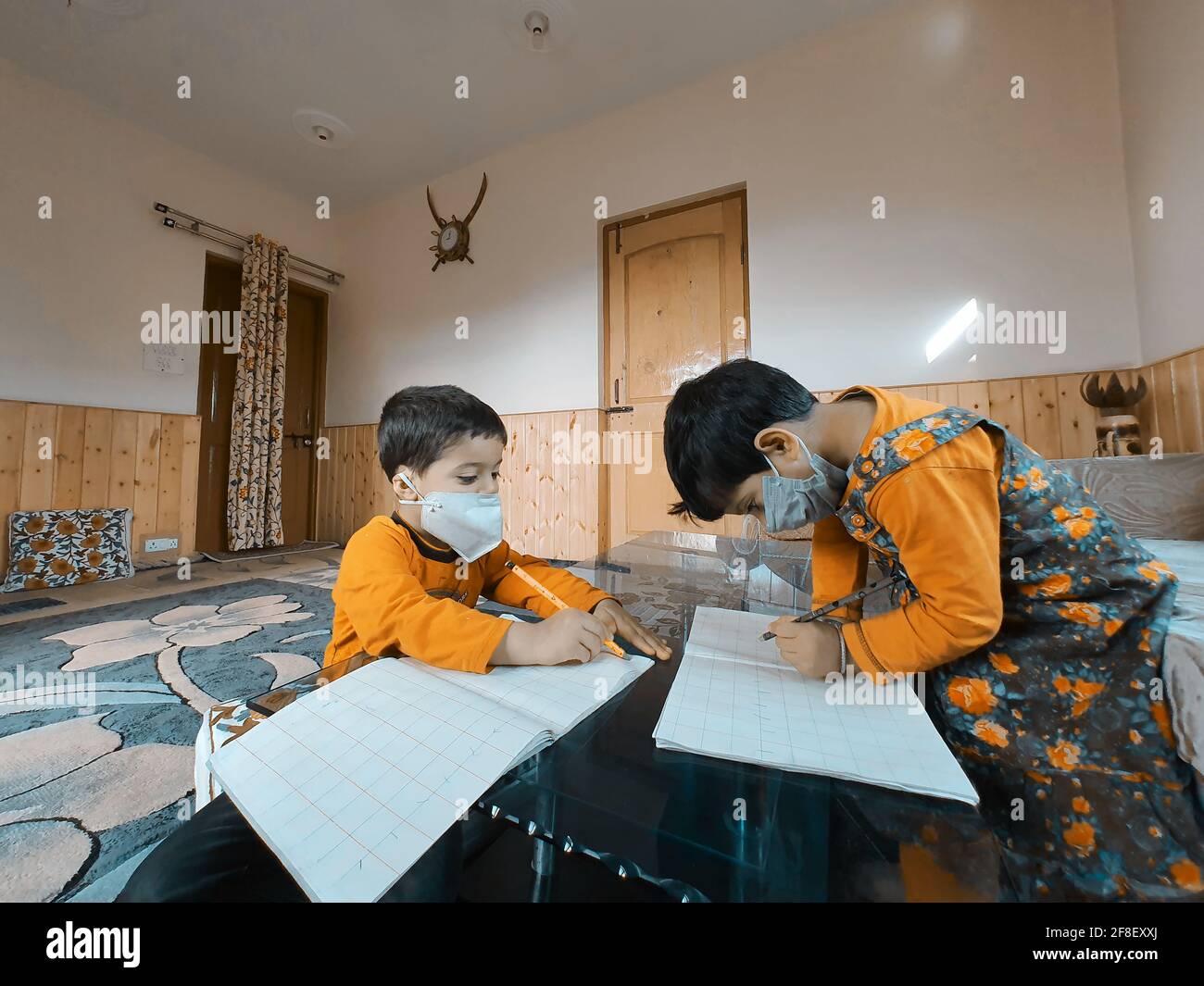 Students wearing masks reading and writing their school work at home during the pandemic coronavirus. Online classes are common due to covid 19. Stock Photo