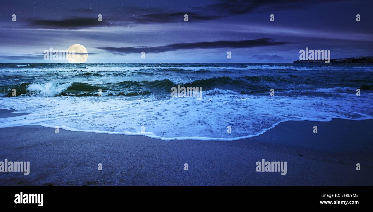 sea tide on a cloudy sunrise. green waves crashing golden sandy beach in  full moon light. storm weather approaching. summer holiday concept Stock  Photo - Alamy