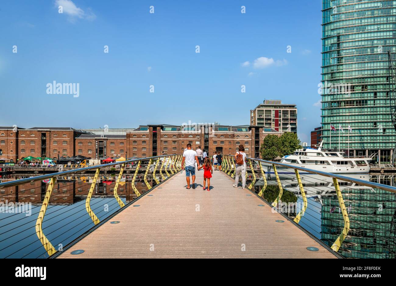 London / UK - August 23 2019: People walk on the North Dock pedestrian bridge that spans the North Dock in Canary Wharf Estate. The old warehouses of Stock Photo