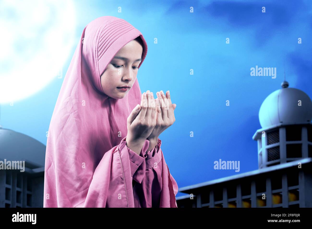 Asian Muslim woman in a veil standing while raised hands and praying ...