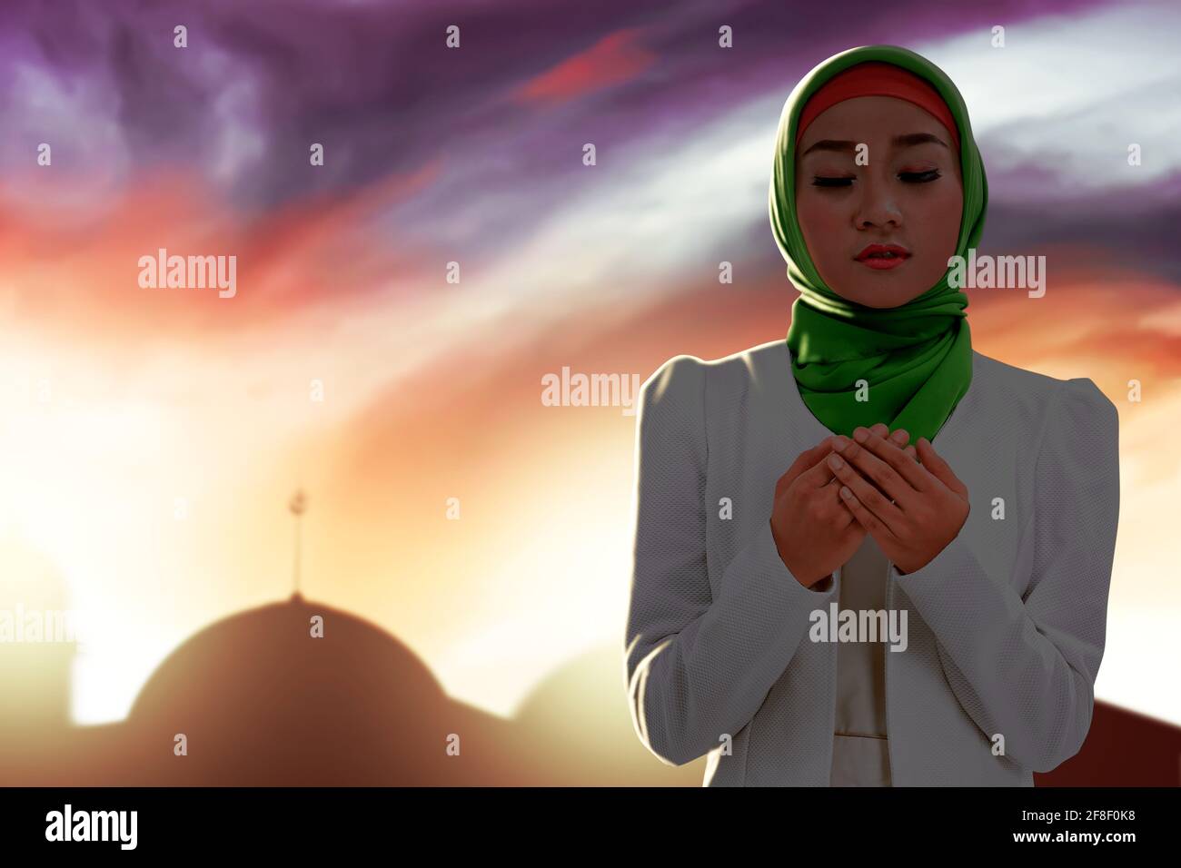 Asian Muslim woman in a veil standing while raised hands and praying ...