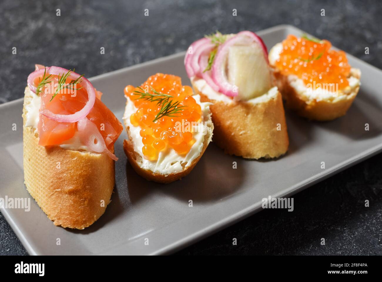 Bruschetta assortment with baguette, cream cheese, red caviar, salmon, herring and onion served on the black stone background. Set of appetizers with Stock Photo