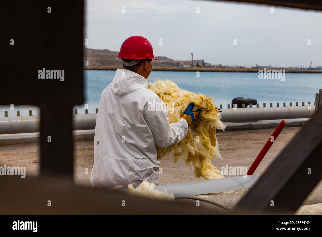 Mangystau. Kazakhstan: Oil loading terminal Bautino Caspian sea. Worker in white protective suit and red hardhat with heat insulator. Isolating pipes. Stock Photo