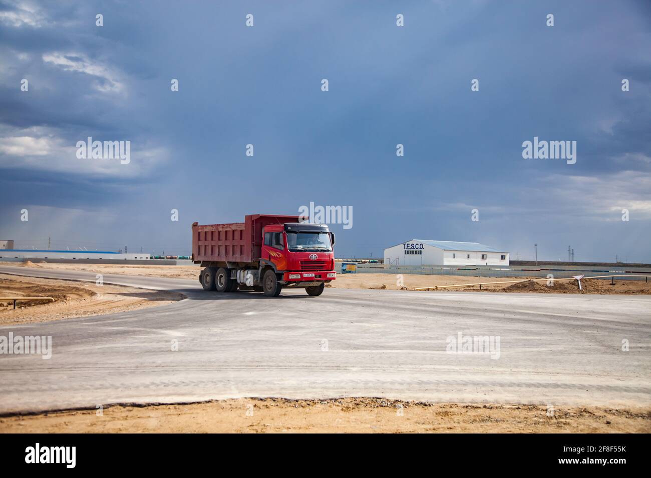 Aktau, Kazakhstan.Red truck FAW on road, and industrial building of TESCO company. Beautiful natural light and storm clouds. Free economic zone. Stock Photo