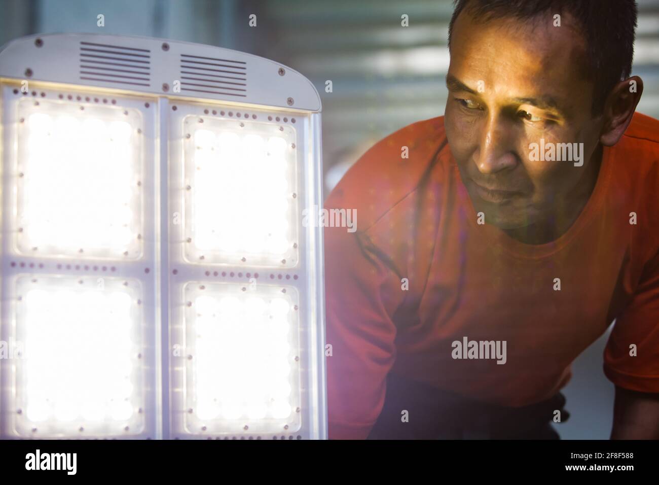 Aktau, Kazakhstan - May 19, 2012: Asian man worker looking at Street illumination LED light panel. Light ON. Light flares (right, center) is out of f Stock Photo
