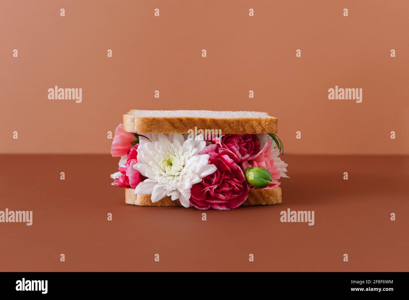 The creative conceptual sandwich is made with various flowers on the pastel background. Minimal summer food theme. Stock Photo