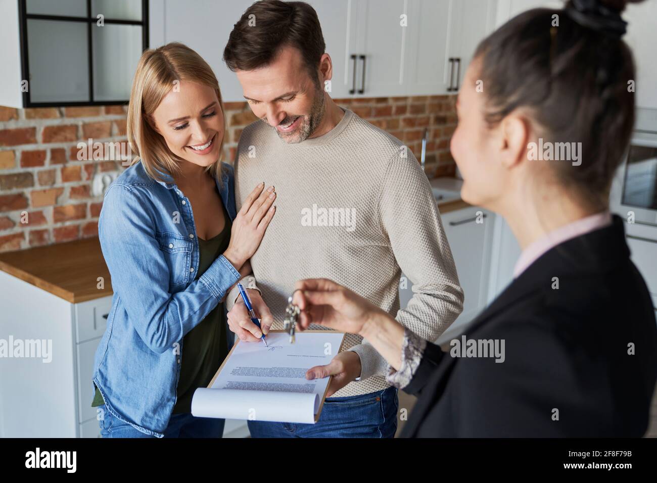 Couple with real estate agent signing contract of new apartment Stock Photo