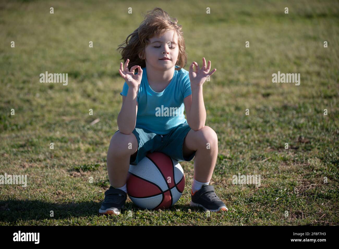 Schoolboy sitting on basketball and relax. Tired kid sports man sitting with basket ball at the playground Stock Photo
