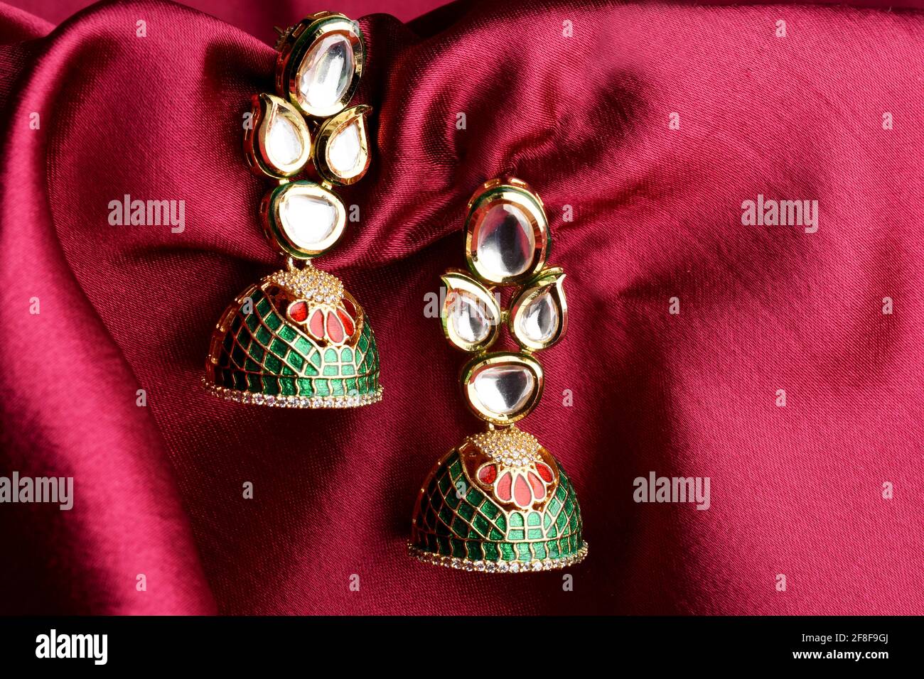 Beautiful Golden pair of earrings Diamonds gemstones on a red satin background Indian traditional jewellery, Bridal Gold earrings wedding jewellery Stock Photo