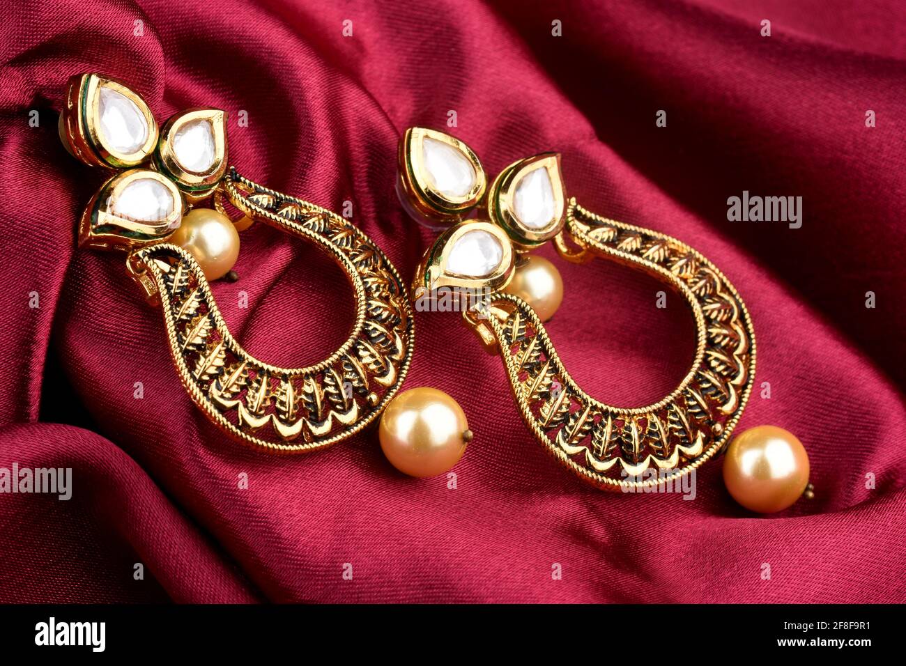 Beautiful Golden pair of earrings Diamonds gemstones on a red satin background Indian traditional jewellery, Bridal Gold earrings wedding jewellery Stock Photo