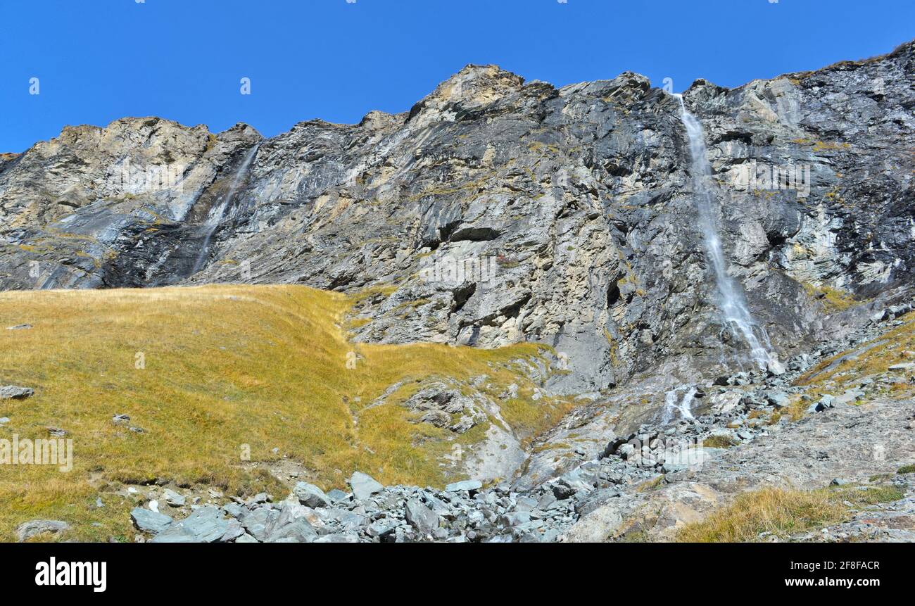 view on waterfall on a stone cliff overlooking a meadow in french Alps ...